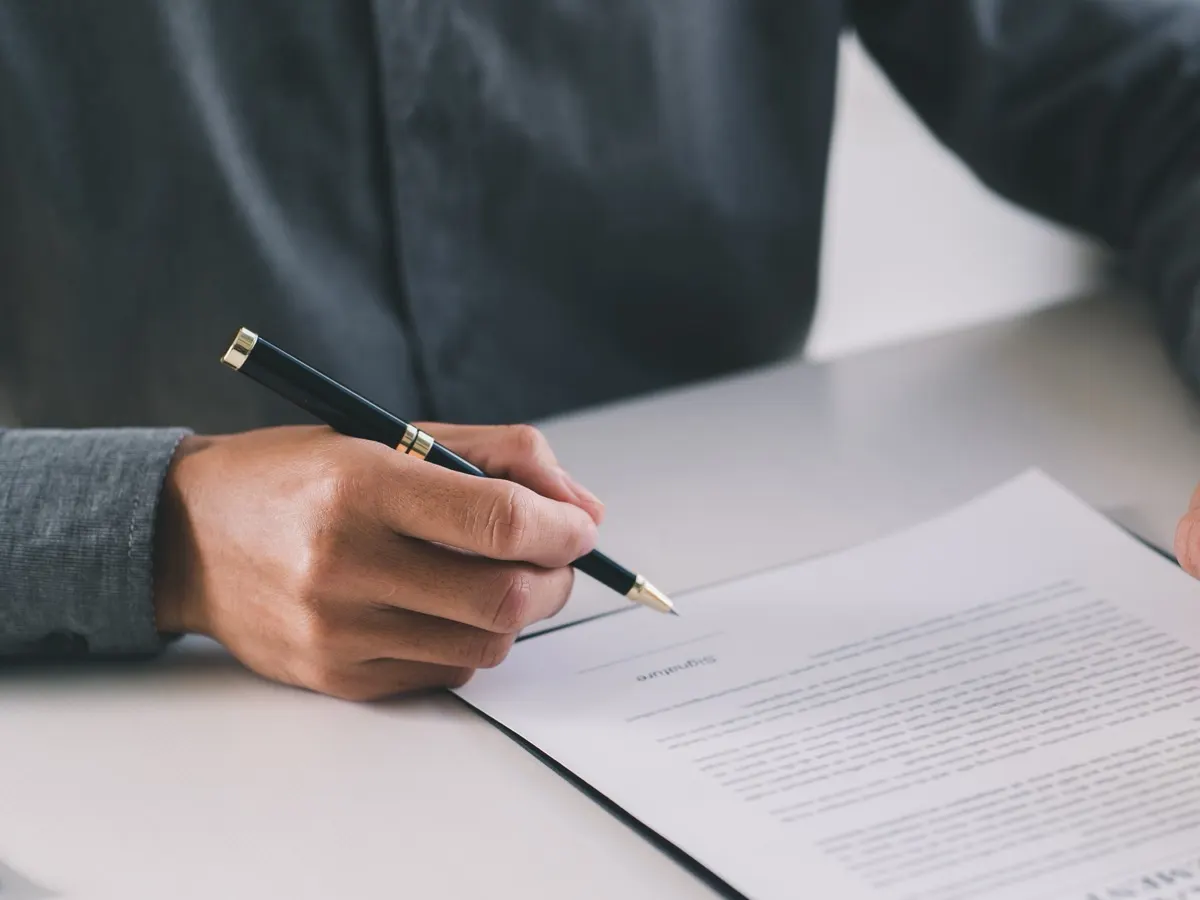 A hand signing a contract at a desk